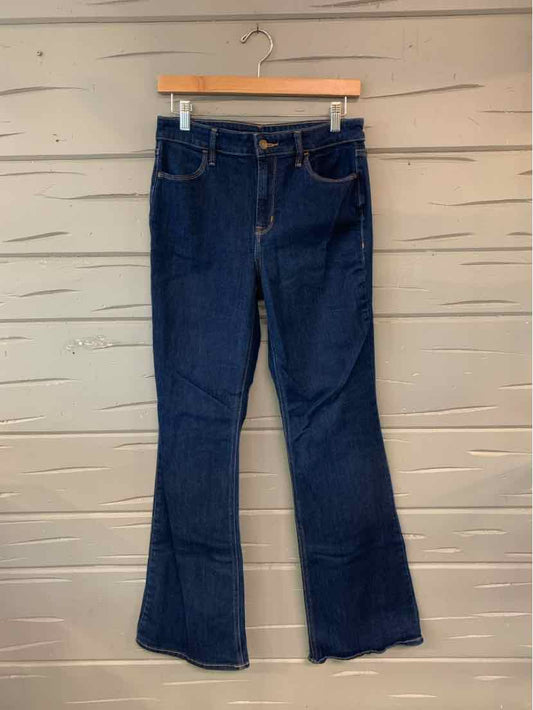 Dark blue denim jeans with slight flare leg, five-pocket design, and visible stitching hanging on wooden hanger against wood .