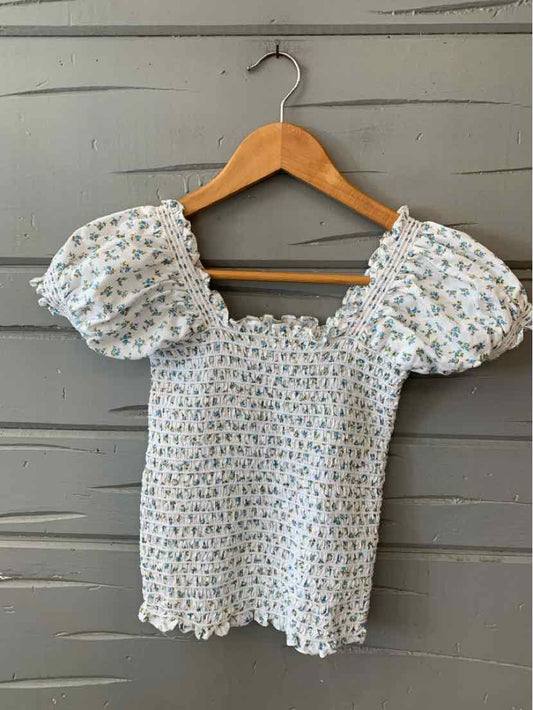 White smocked top with blue floral print and puff sleeves on wooden hanger.