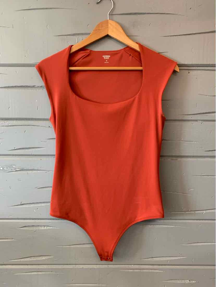 Rust orange sleeveless bodysuit with scoop neckline and fitted silhouette hanging on wooden hanger.