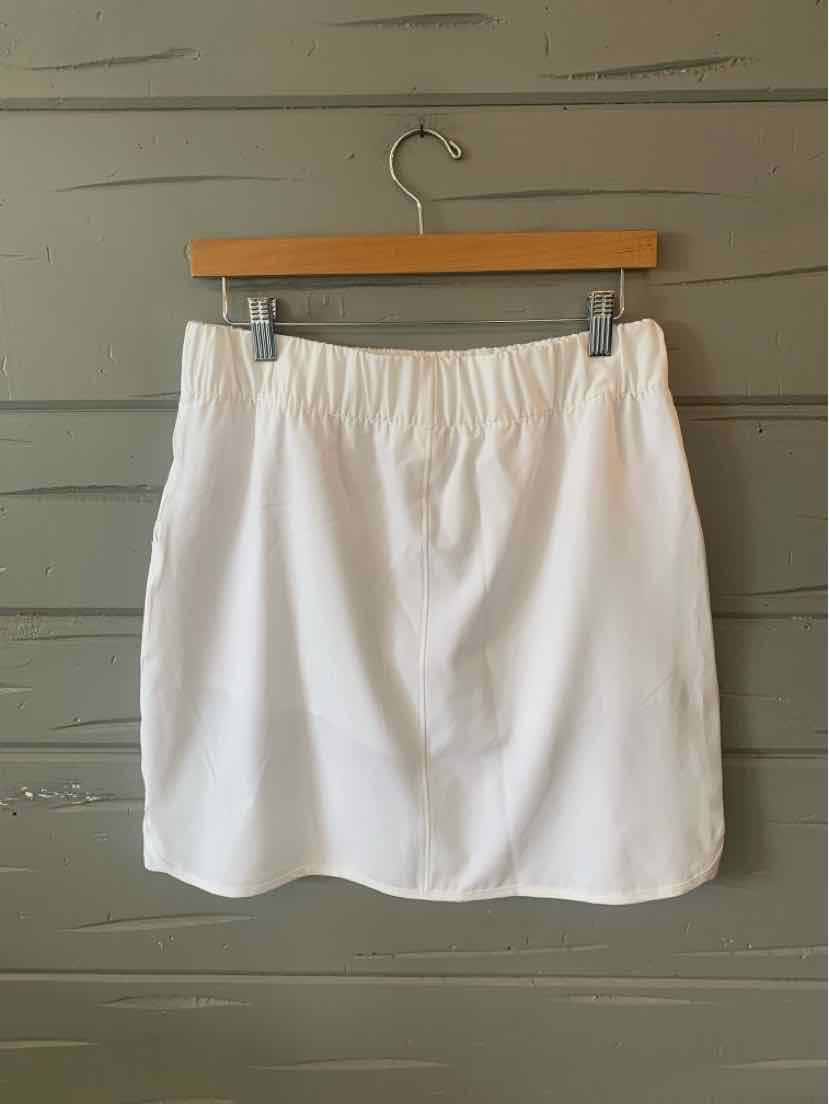 White solid skort with elastic waistband and smooth fabric, hanging on wooden hanger against gray wall.
