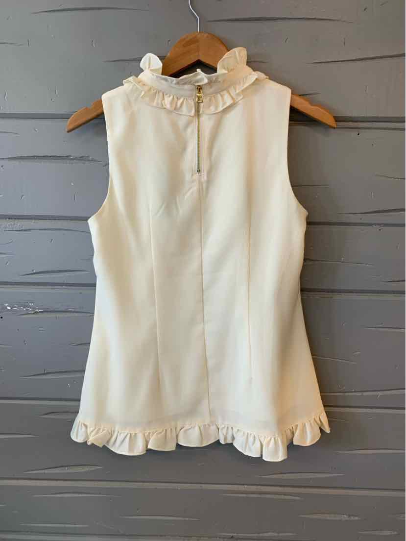 Cream sleeveless top with ruffled collar and hem hanging on wooden hanger.
