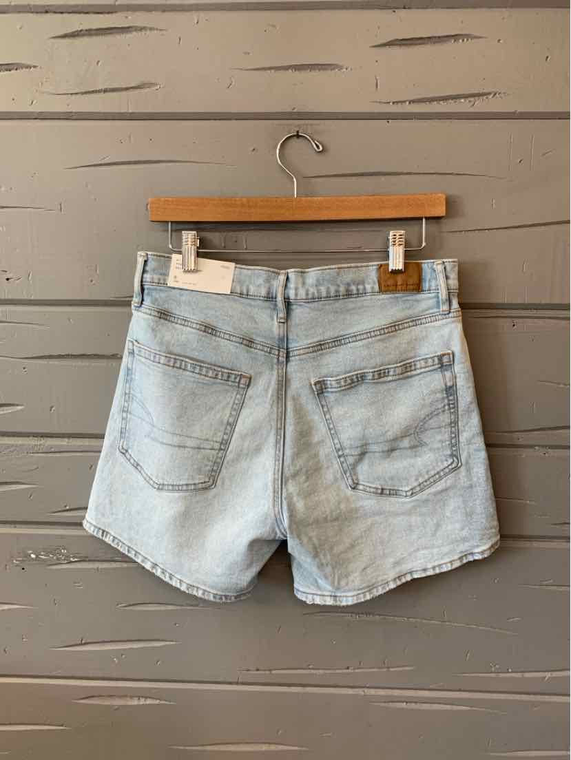 Light blue denim shorts with two back pockets, belt loops, and a frayed hem hanging on a wooden hanger.