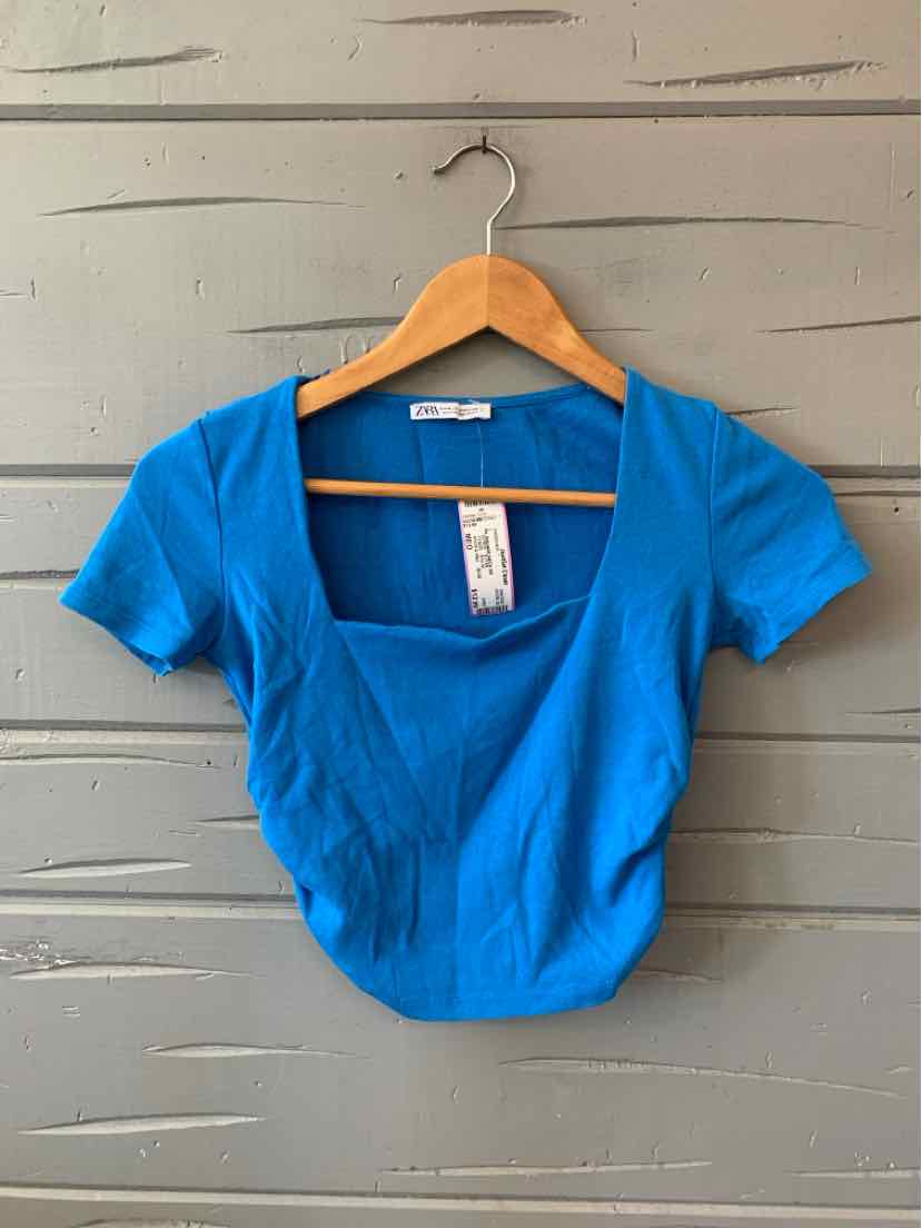 Bright blue cropped short-sleeve top with square neckline and fitted silhouette on wooden hanger.