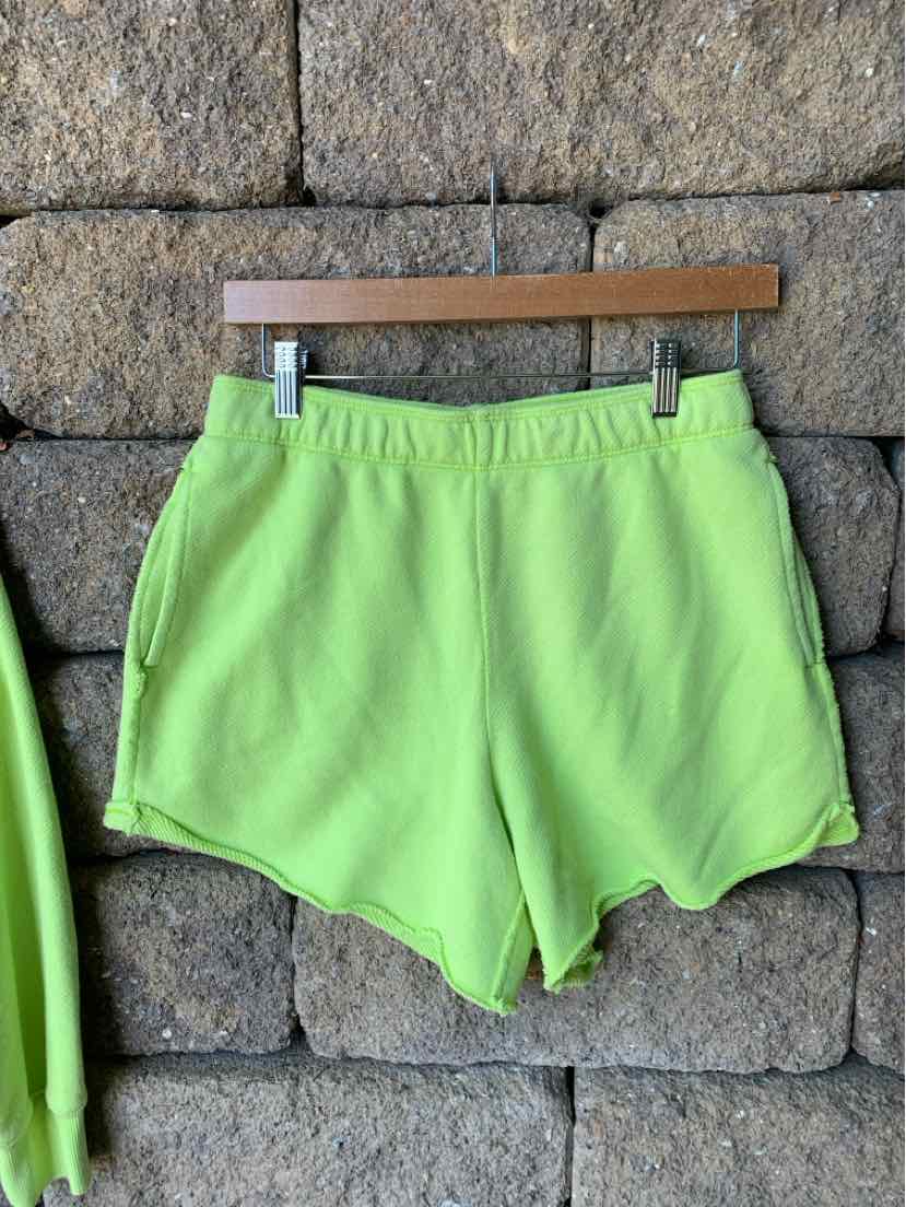 Light green soft fabric shorts with elastic waistband and curved hem hanging on wooden hanger.