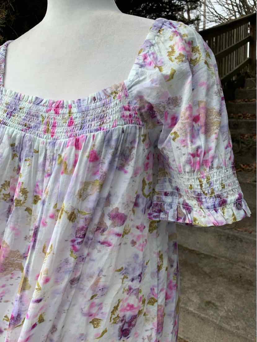 White cotton dress with pink and yellow floral print, smocked bodice, square neckline, and puffed sleeves with ruffled cuffs.