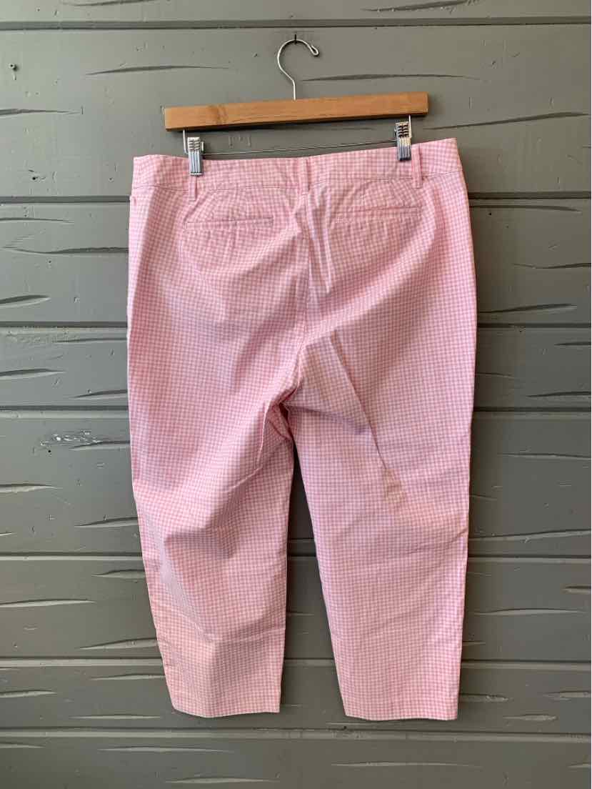 Light pink cropped pants with back pockets hanging on wooden hanger against gray wooden wall.