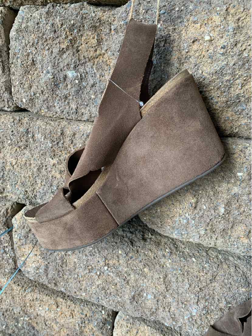 Brown suede wedge sandals with an open toe and ankle strap on stone background.