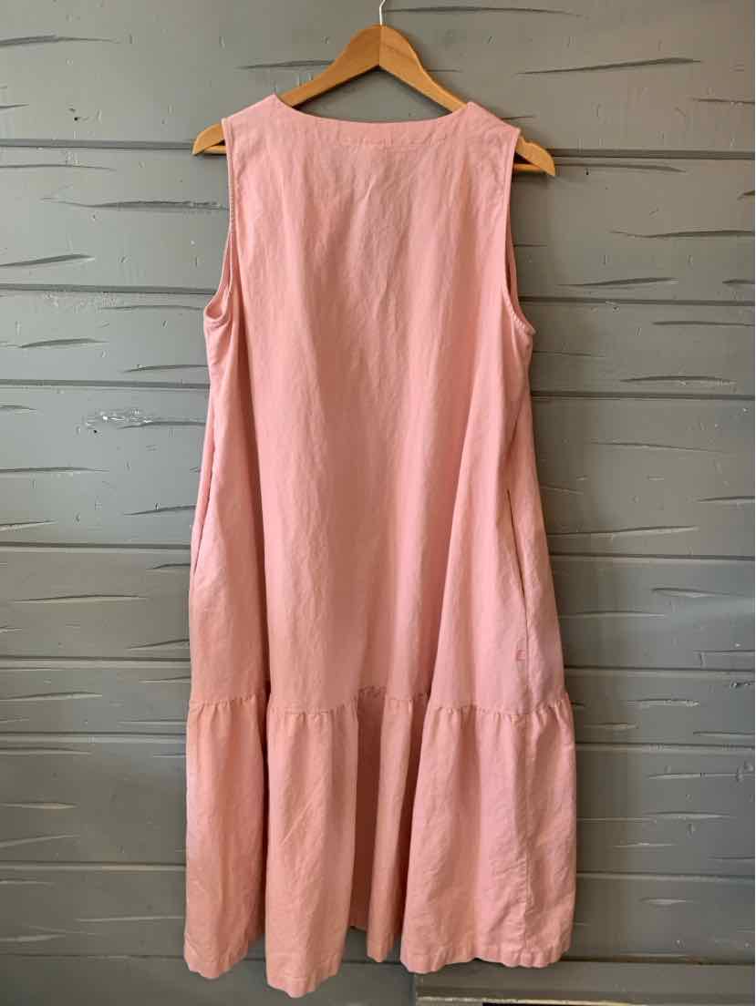 Sleeveless light pink dress with loose fit and tiered ruffle hem, hanging on wooden hanger.