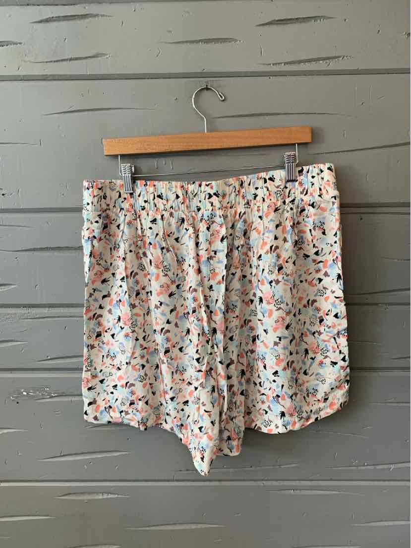 White shorts with a multicolor abstract pattern, relaxed fit, hanging on wooden hanger.