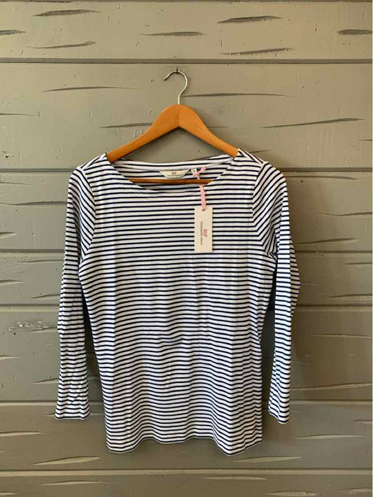 Women’s long-sleeve white shirt with navy horizontal stripes hanging on wooden hanger against a gray wooden wall.
