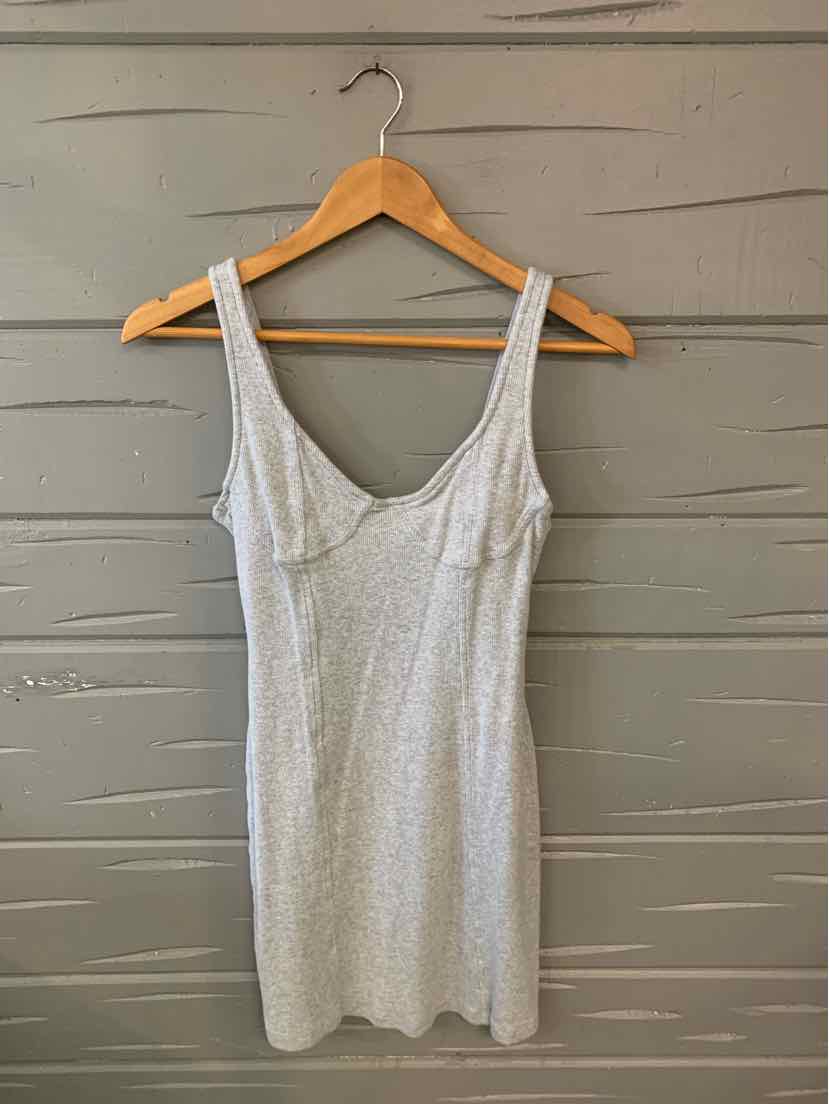 Light gray sleeveless knit dress with scoop neckline hanging on wooden hanger against gray wooden wall.