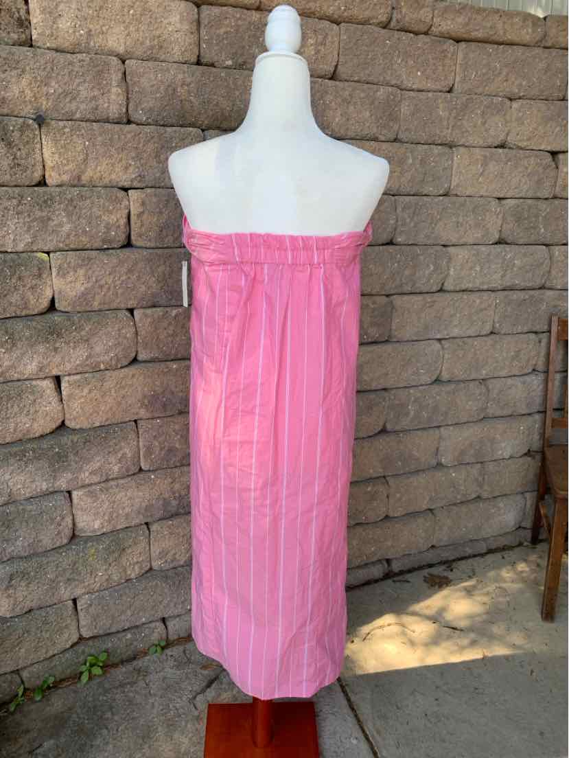 Pink strapless maxi dress with vertical stripes and ruffled elastic neckline displayed on mannequin against stone wall.