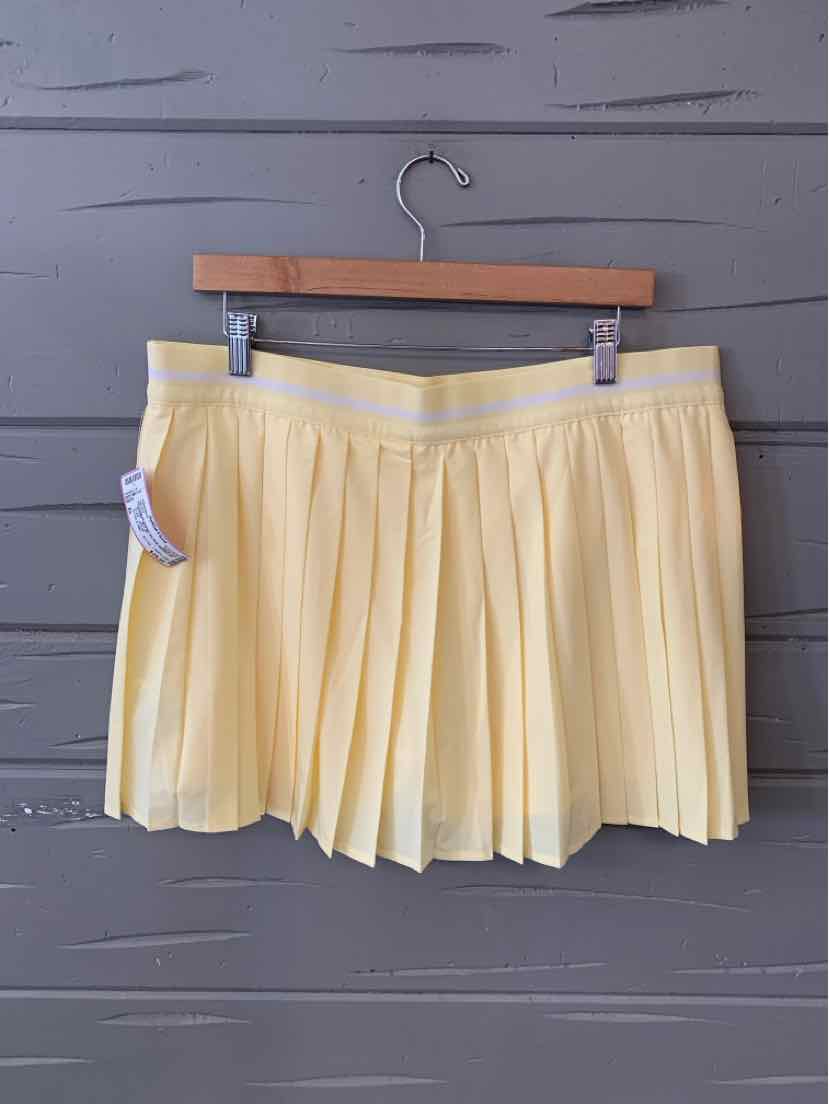 Yellow pleated skort with elastic waistband hanging on wooden hanger against gray wall.