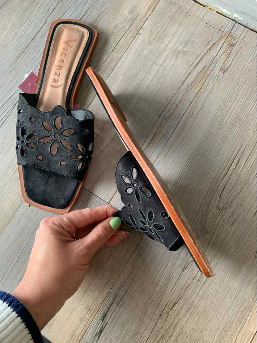 Black flat slide sandal with laser-cut floral design and tan sole, size 10.