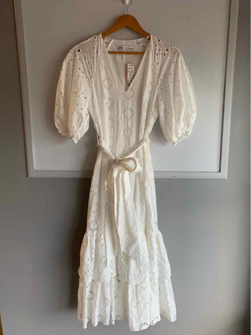 White midi eyelet dress with puff sleeves, V-neckline, and waist tie belt hanging on wooden hanger.