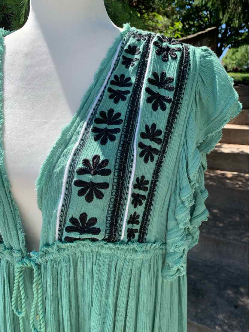 Light green sleeveless dress with black floral embroidery and ruffled edges on lightweight fabric.