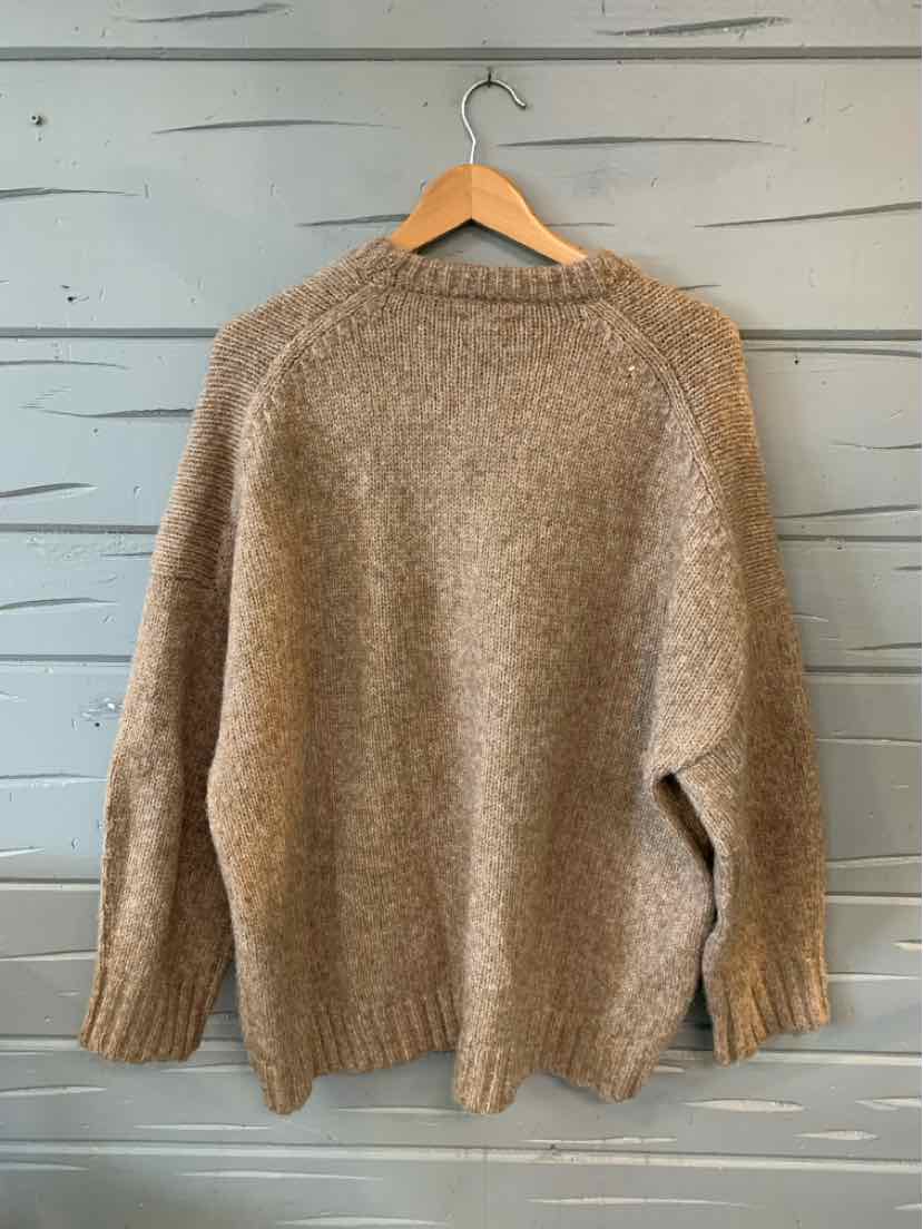Tan knit sweater with long sleeves and ribbed cuffs on wooden hanger.