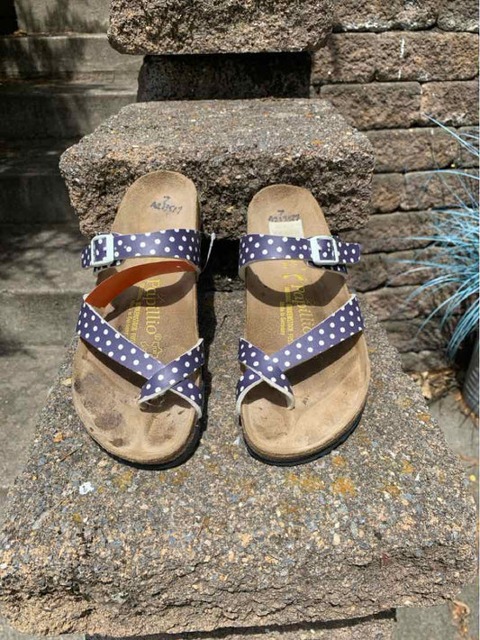 Navy blue sandals with white polka dot fabric straps and adjustable buckles on cork footbeds.
