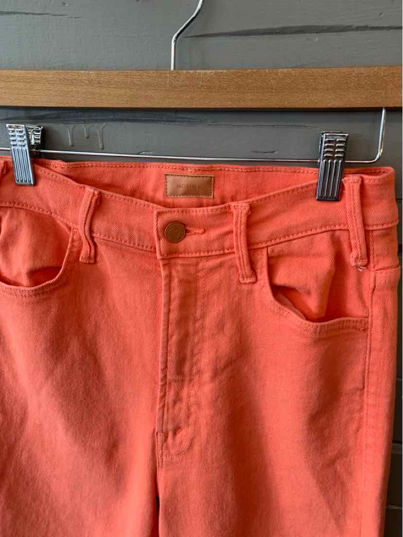 Coral orange high-waist jeans with front button and pockets, hanging on wooden hanger.
