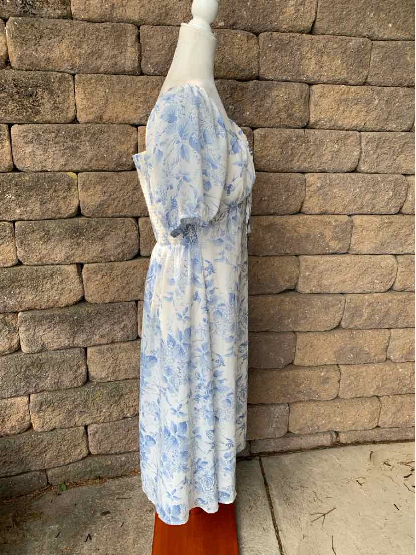 Light blue and white floral midi dress with short puff sleeves and cinched waist on mannequin against stone wall background.