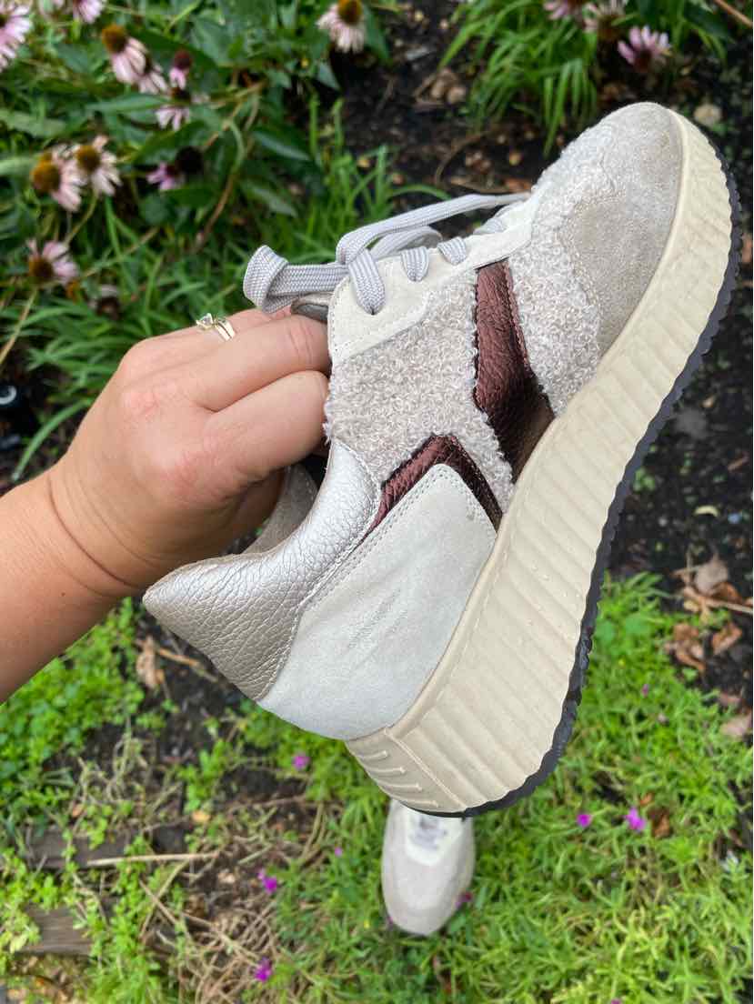 Beige sneaker with textured suede and smooth leather panels, featuring white laces and a thick, ridged sole.