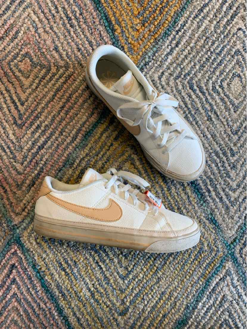 White and beige Nike sneakers with beige swoosh logo and white laces in size 8 on patterned carpet.