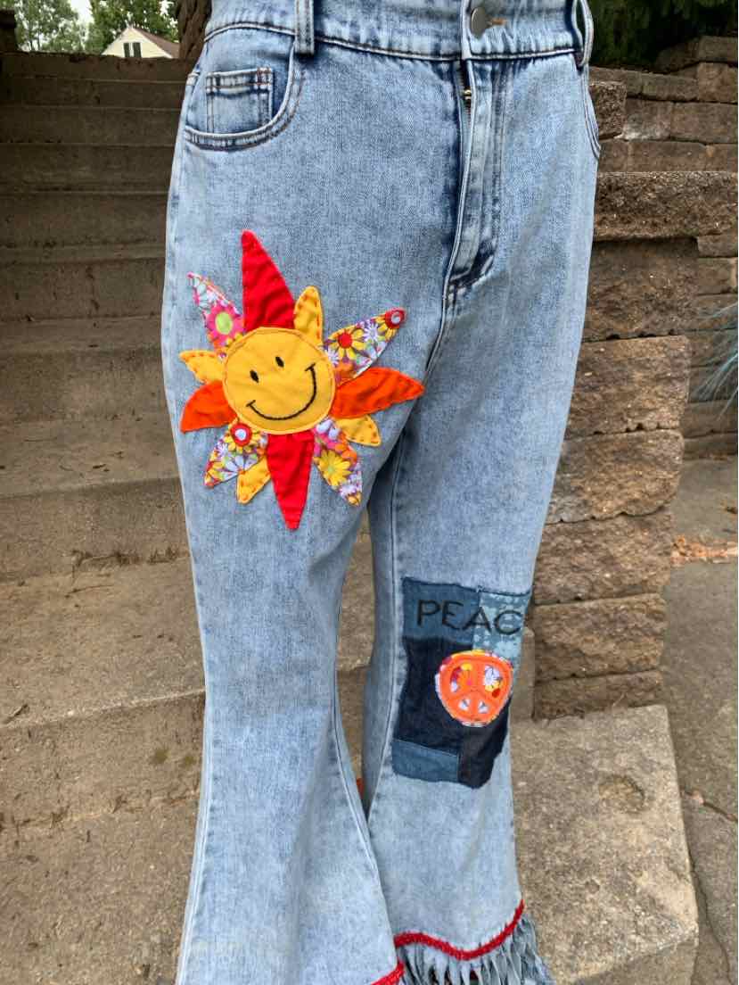Light blue denim jeans with a colorful smiling sun patch and a dark blue patch featuring "PS" and an orange fish on the.