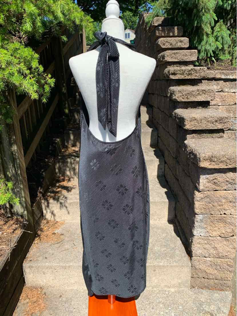 Black halter neck dress with subtle floral pattern and open back, knee-length design.
