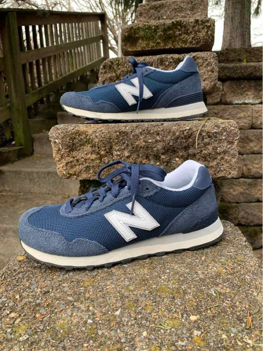 Navy blue New Balance sneakers with white "N" logo and beige sole on stone steps.