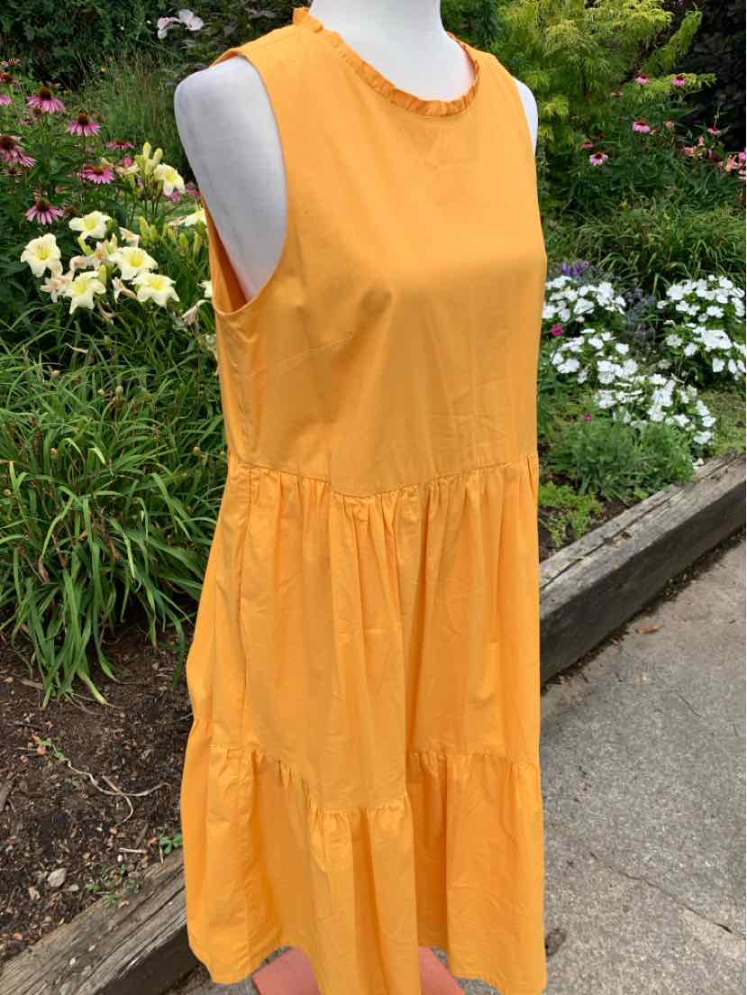 Sleeveless orange cotton dress with tiered skirt and round neckline displayed outdoors.