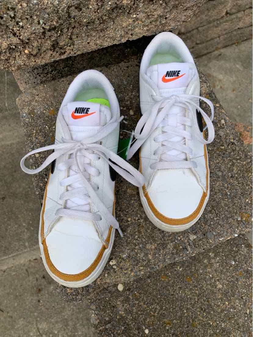 White Nike low-top sneakers with orange swoosh logo, white laces, and tan accents on toe.