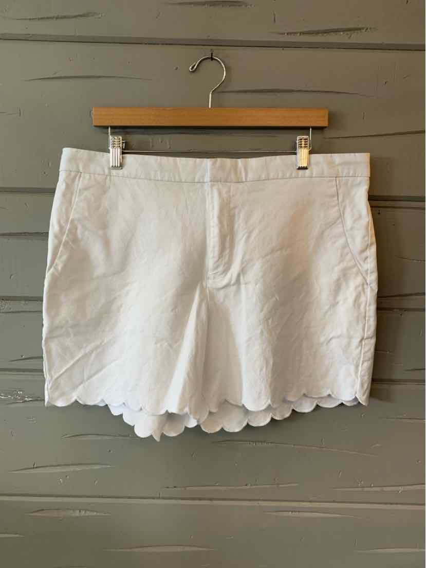 White cotton shorts with scalloped hem and front zipper closure hanging on wooden hanger.
