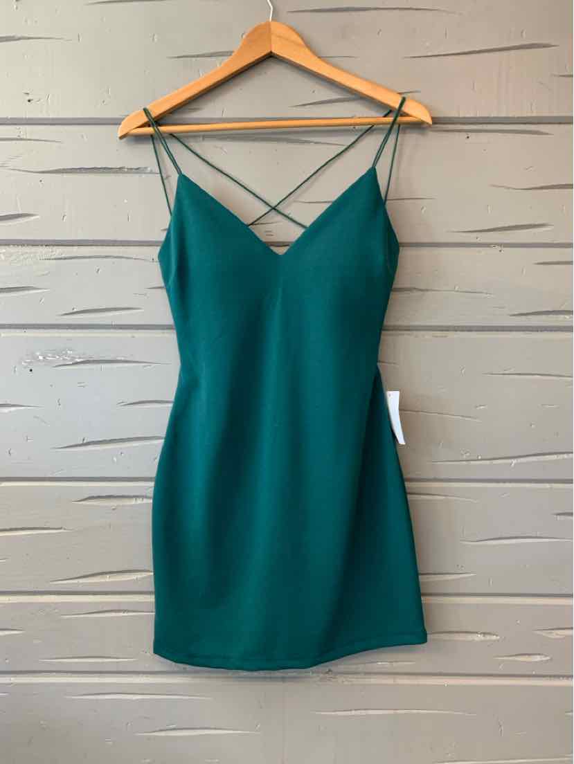 Green sleeveless mini dress with thin crisscross straps and a V neckline on wooden hanger.