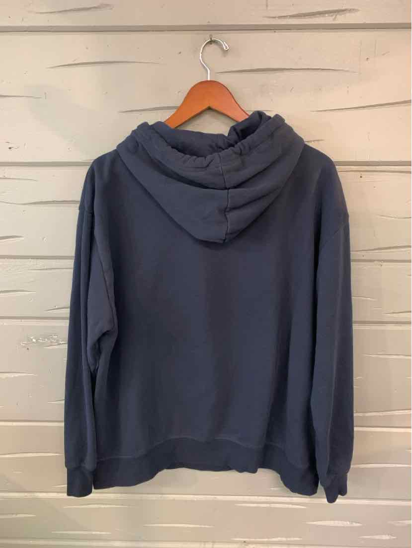 Navy blue oversized hoodie with front pocket and drawstring hood on wooden hanger against white shiplap wall.