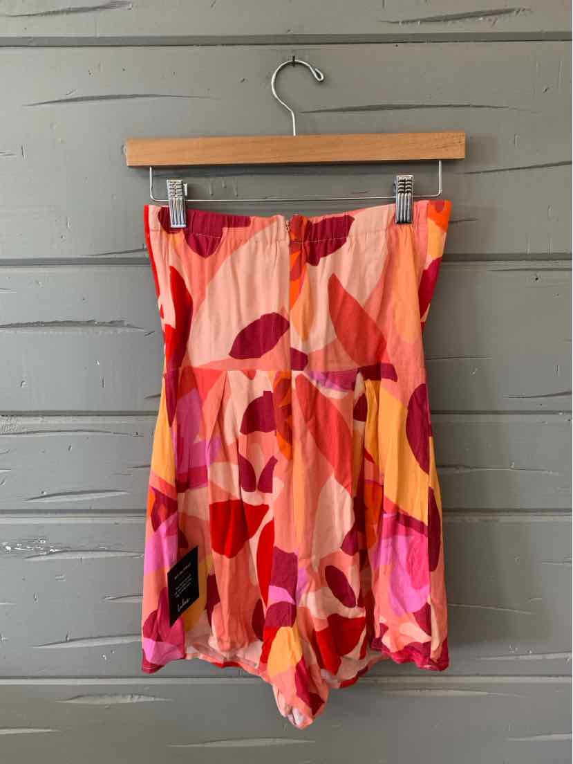 Colorful striped romper in shades of pink, red, orange, and yellow with a strapless, fitted bodice and loose shorts.