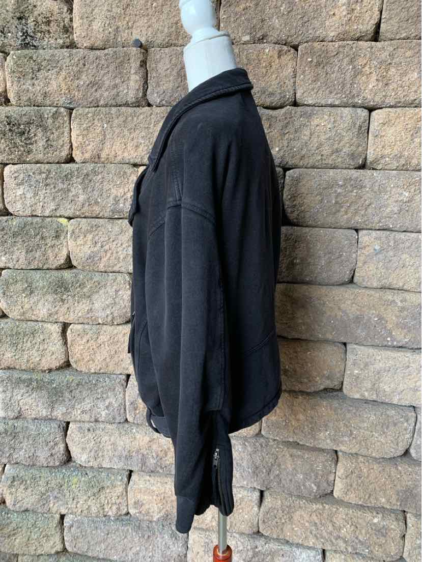 Black long-sleeve sweatshirt with a relaxed fit and ribbed cuffs, shown on a mannequin against a stone wall background.