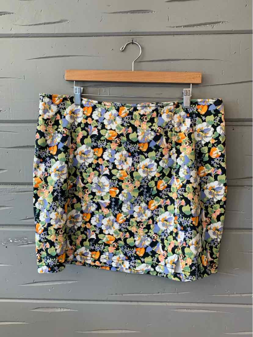 Mini skirt with colorful floral print on black background hanging on wooden hanger.