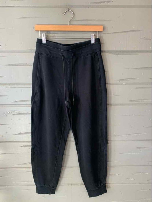 Black jogger pants with a relaxed fit, elastic cuffs, and a gathered waistband, hanging from a wooden hanger.