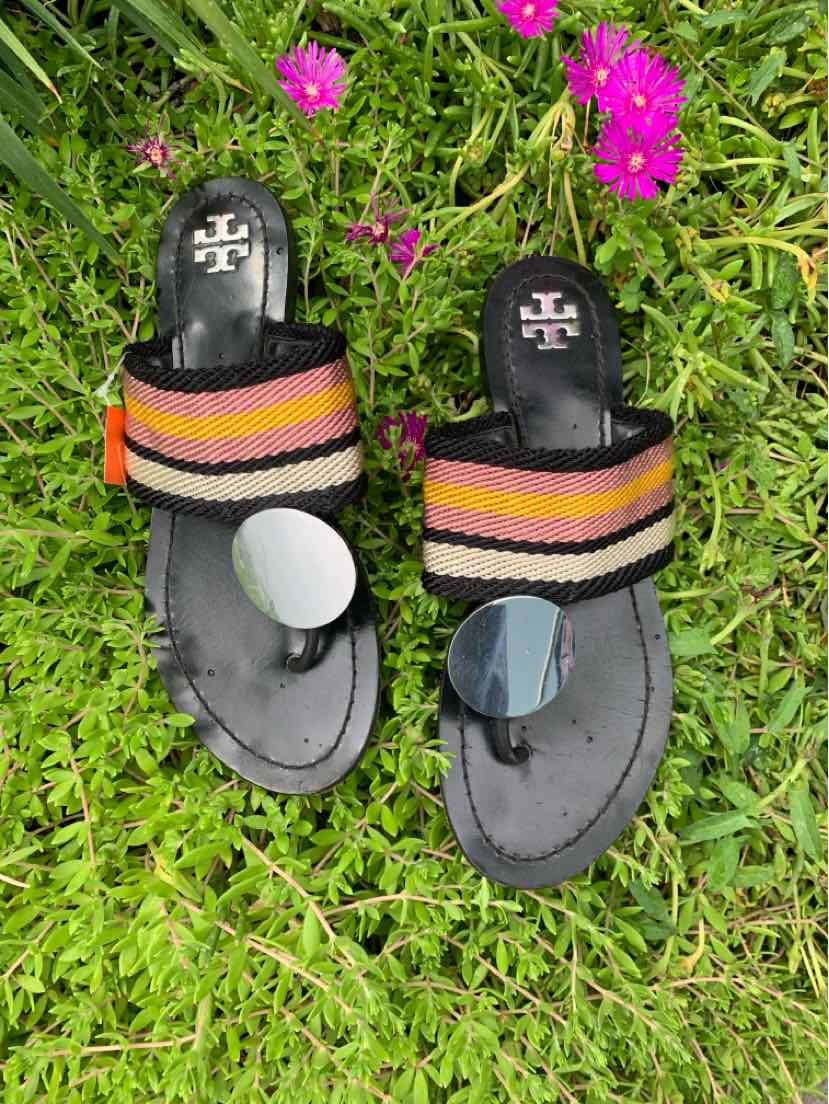 Black Tory Burch sandals with multicolored woven straps in orange, pink, and yellow on grassy background.
