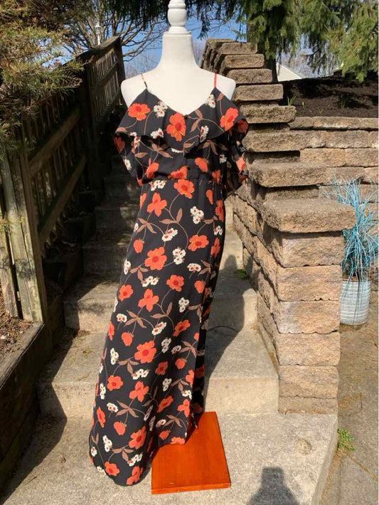 Black maxi dress with red and white floral print, thin shoulder straps, and ruffled neckline on mannequin outdoors.