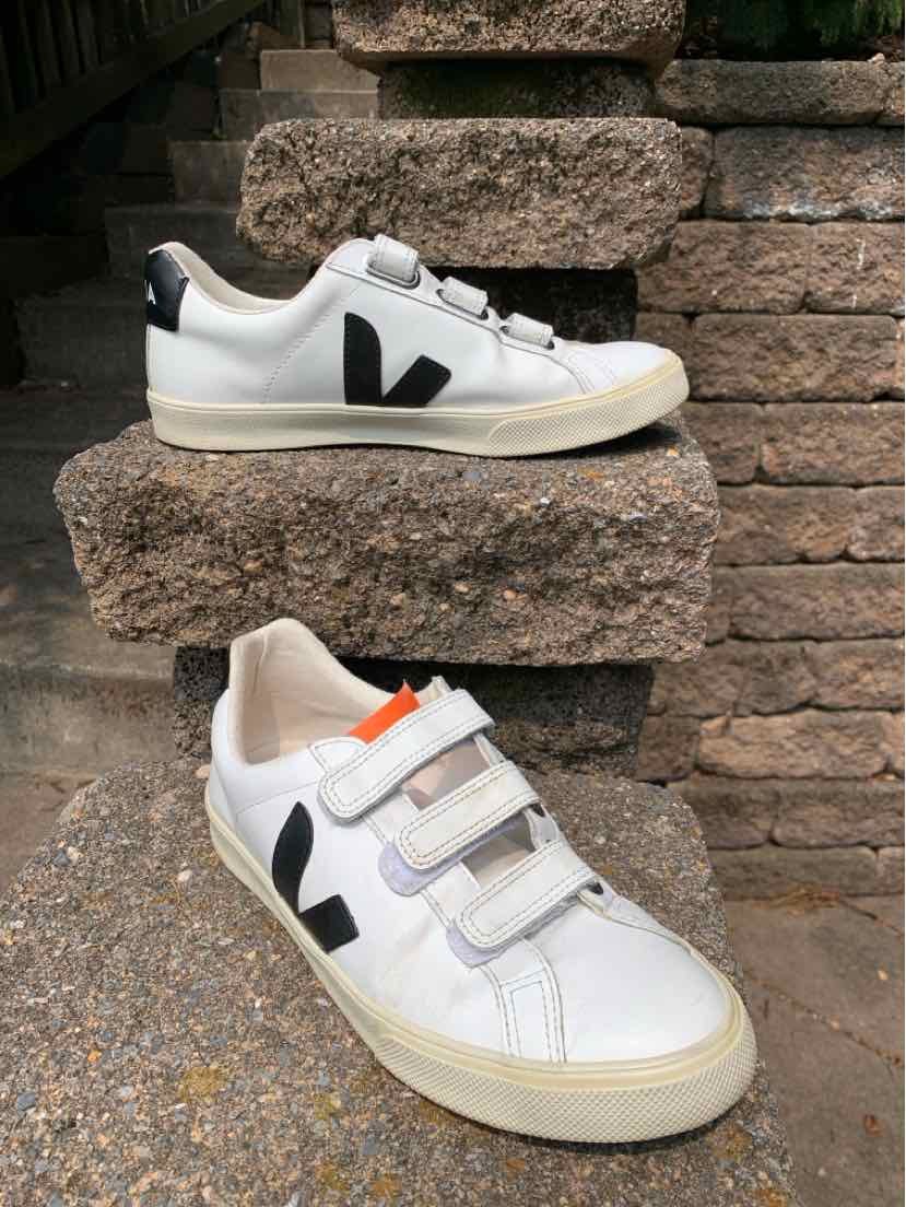 White low-top sneaker with black V logo, three velcro straps, and a slightly off-white sole.