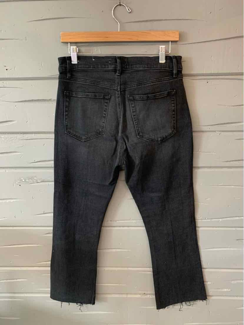 Black cropped jeans with a raw hem and back pockets, size 6, hanging on a wooden hanger.