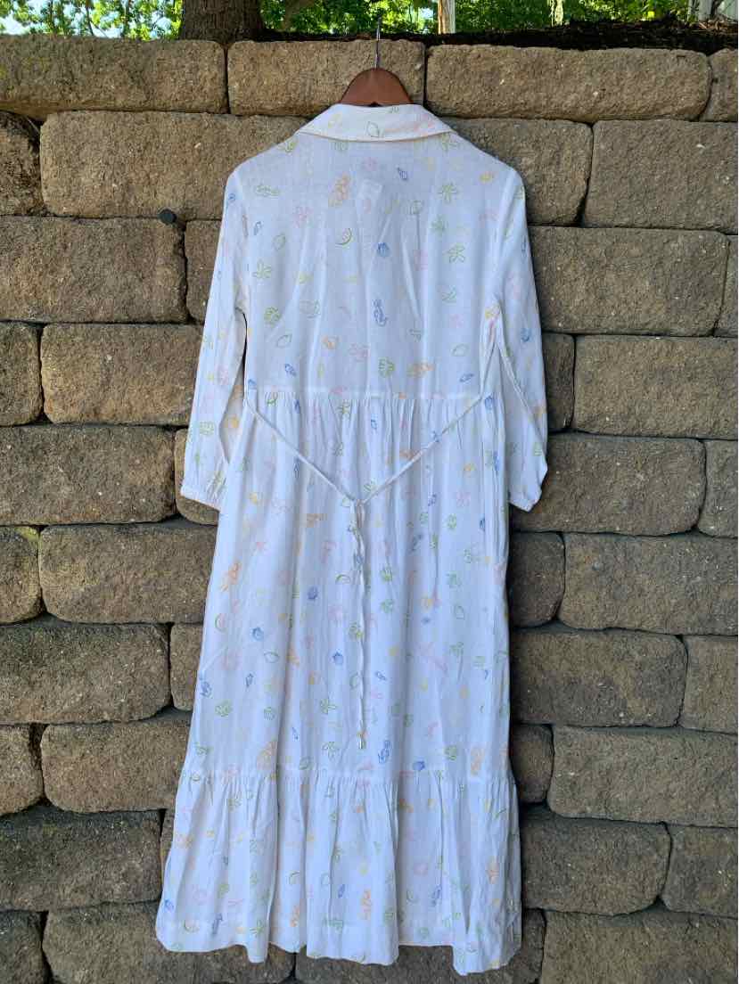 White long-sleeve midi dress with a loose fit, subtle yellow floral print, and tiered skirt.
