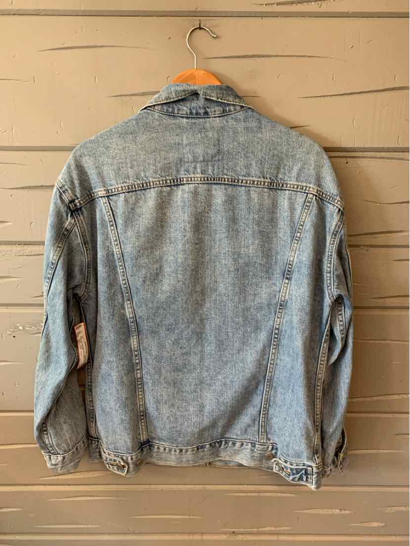 Light blue faded denim jacket with long sleeves and classic collar hanging on wooden hanger against beige wooden wall.