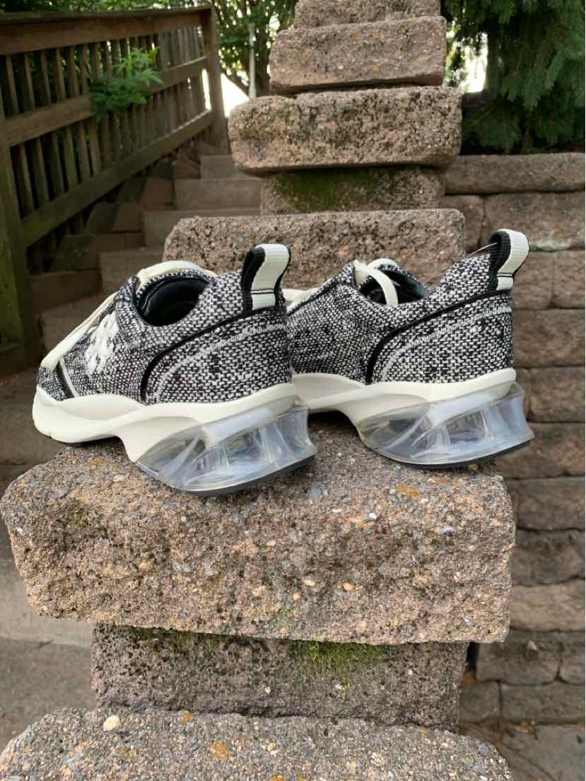 Black and white tweed sneakers with thick translucent curved soles and pull tabs at heel and tongue.