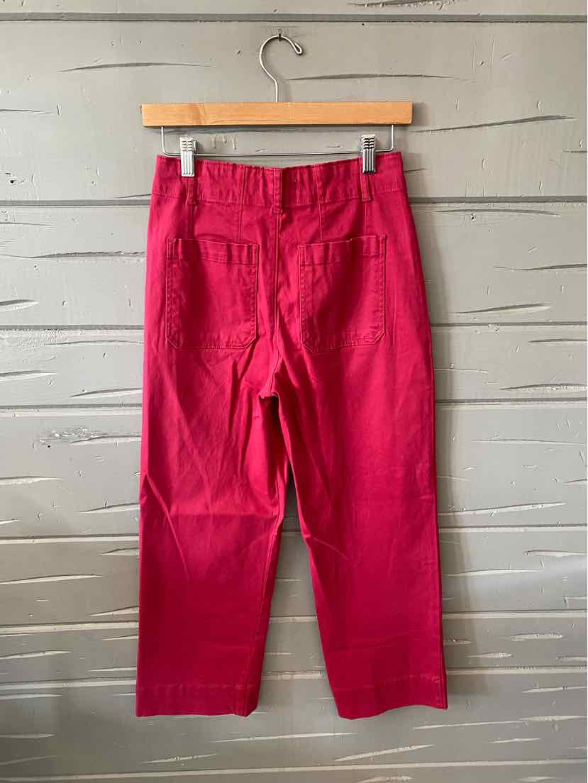 Bright red high-waist pants with straight legs and back pockets on wooden hanger against rustic wall.