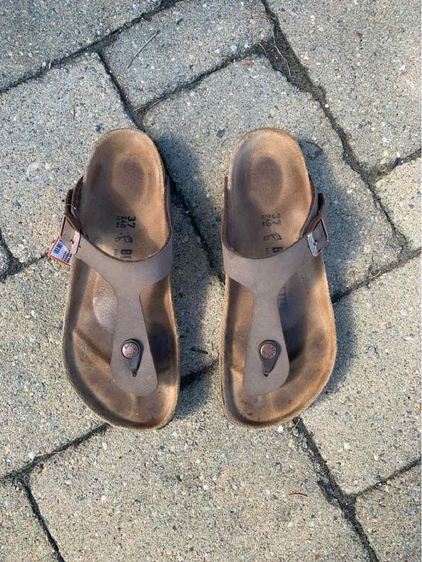 Brown leather Birkenstock sandals with adjustable straps and contoured footbeds on stone pavement.