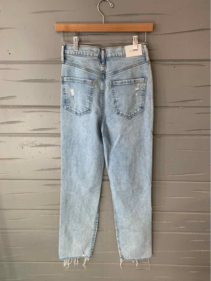 Light blue high-waist denim jeans with frayed hems and back pockets hanging on a wooden hanger.