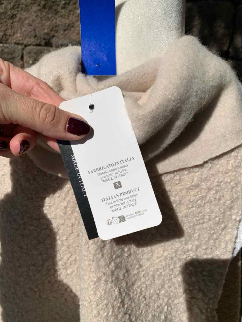 Beige bouclé knit garment with a white product tag attached by a blue ribbon.