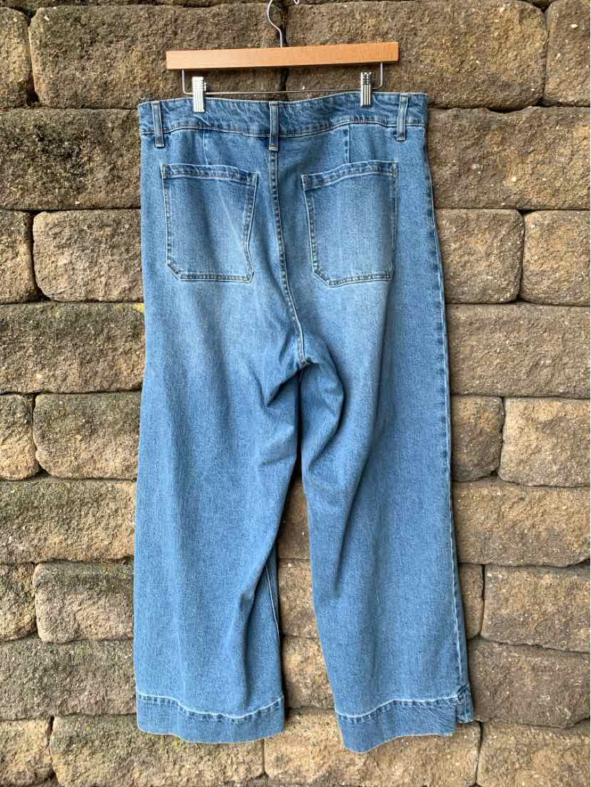Light blue high-waist denim jeans with wide legs and back patch pockets hanging on a wooden hanger.